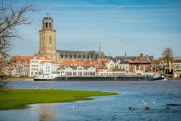 Historisch stadsbeeld met de toren van Deventer en een rustige rivier.