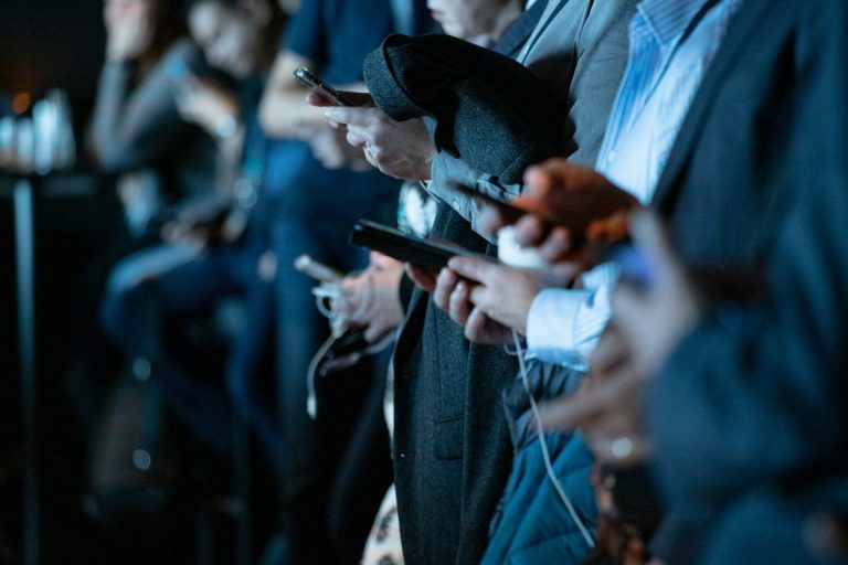 Handen met smartphones en earplugs, mensen staan in een rij bij een evenement.