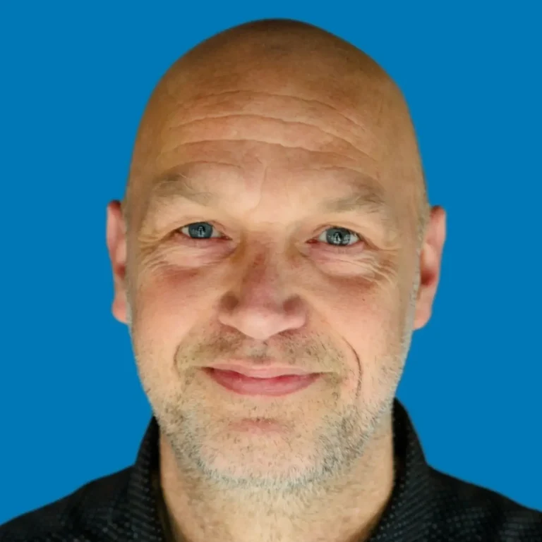 Bald man with a friendly expression and blue background.