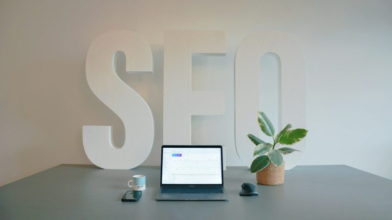 SEO met laptop Laptop op een tafel met een grote "SEO" achterwand en een groene plant.